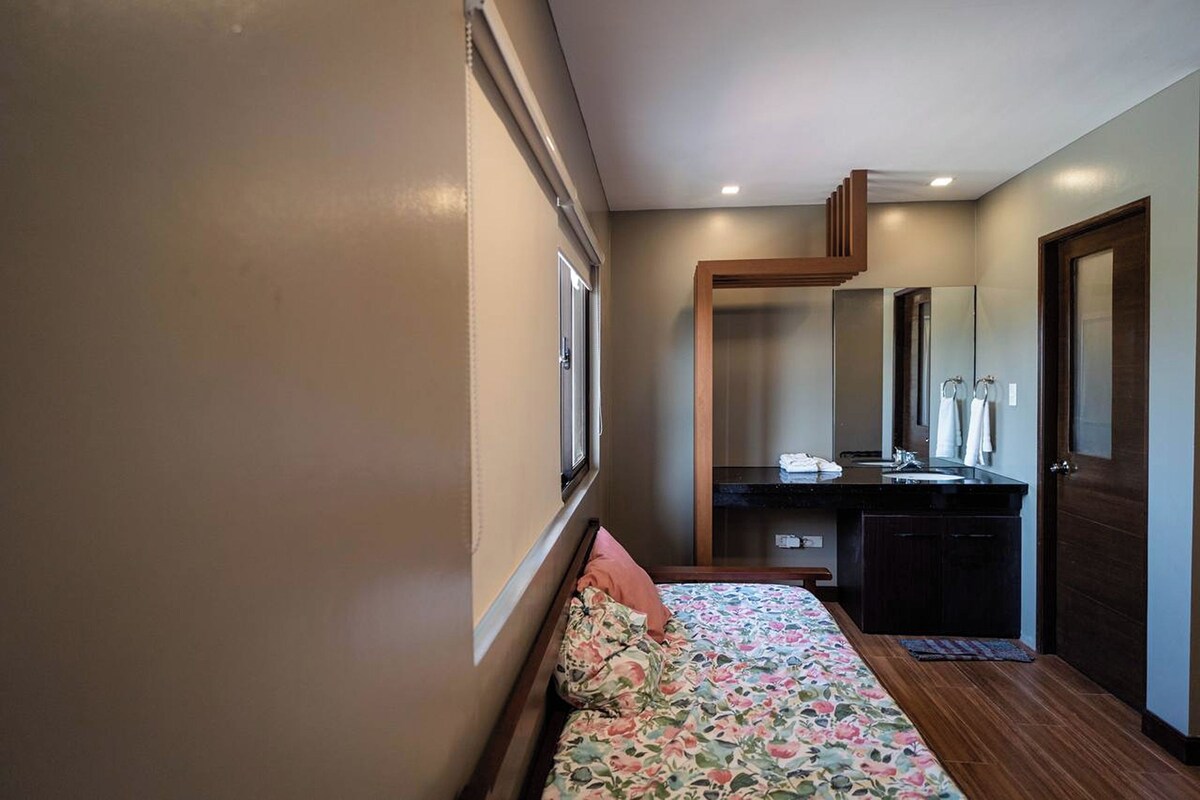 A bedroom with a bed, a bedside table, a mirror, a dresser, and a door.