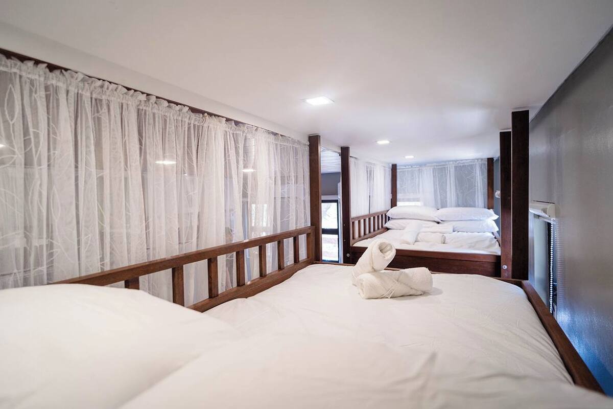 A hotel room with two beds, white linens, wooden headboards, and sheer curtains.