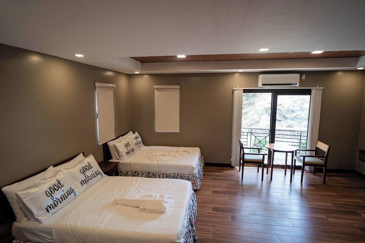 A hotel room with two beds, a balcony, and a small table with chairs.