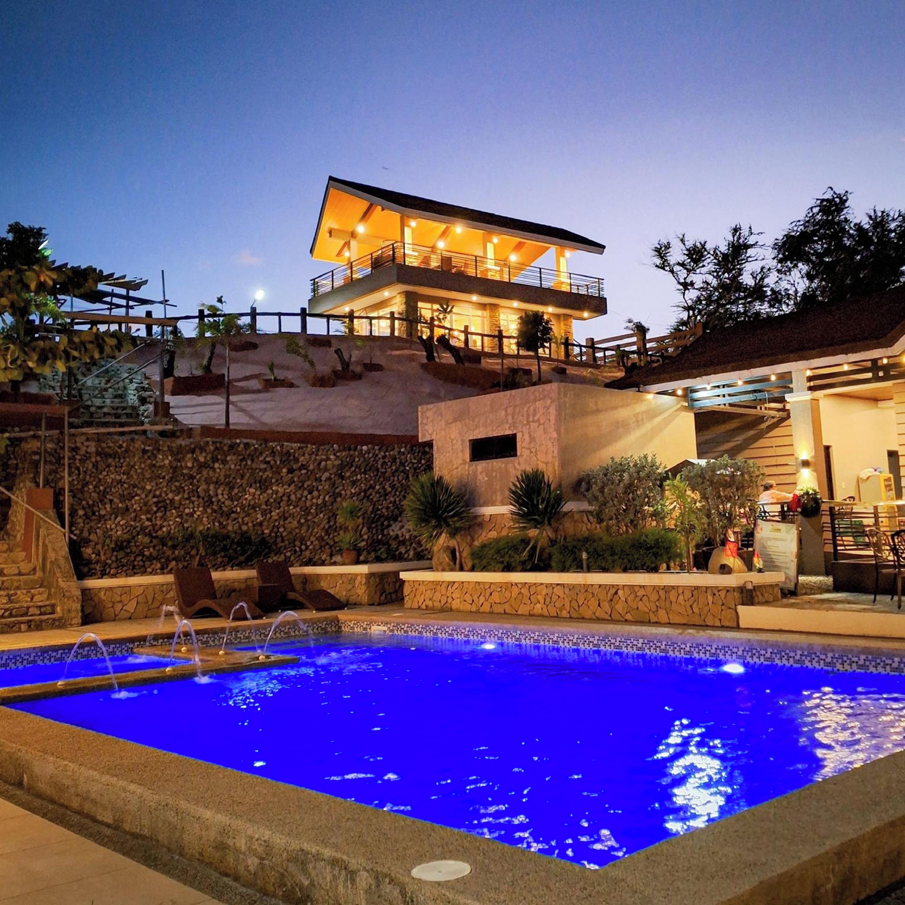 A pool area with a stone wall, a lounge chair, and a building with a balcony.