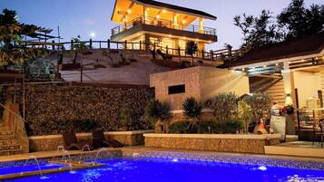 A pool area with a stone wall, a lounge chair, and a building with a balcony.