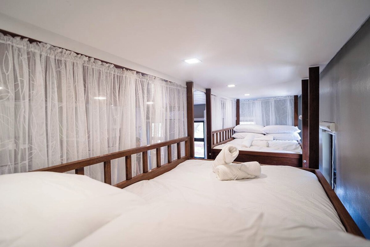Ein Hotelzimmer mit zwei Betten, weißen Laken, Holz-Kopfteilen und transparenten Vorhängen.