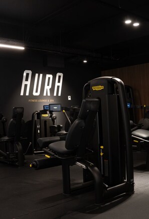 Uma sala de ginástica com um aviso fixado na parede que diz "AURA FITNESS LOUNGE & SPA".