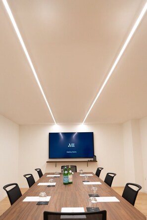 A conference room with a long table, black chairs, a flat-screen TV on the wall, and two bottles of water on the table. - Arbed Living Hotel Self Check-in (Arbedo-Castione)