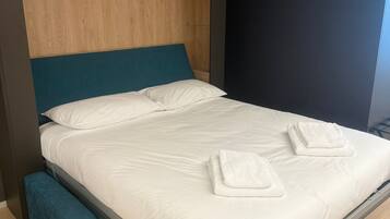 Un lit moderne avec une tête de lit en bois, un banc au pied du lit et un mur foncé sur le côté droit.