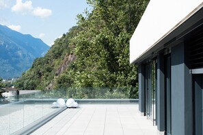 A modern building with a glass balcony overlooking a mountainous landscape.