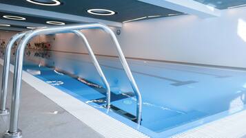 Une piscine avec un escalier en métal, un sol carrelé et un plafond doté de luminaires circulaires.