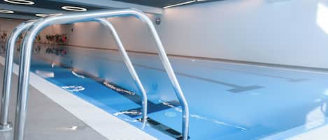 A swimming pool with a metal ladder, tiled floor, and a ceiling with circular lights.