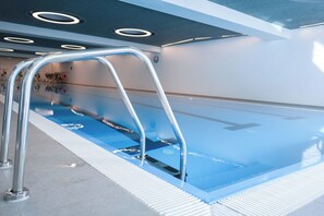 A swimming pool with a metal ladder, tiled floor, and a ceiling with circular lights.