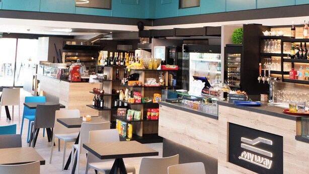 A modern restaurant with teal cabinets, a bar area, and a seating arrangement with tables and chairs. - Arbed Living Hotel Self Check-in (Arbedo-Castione)