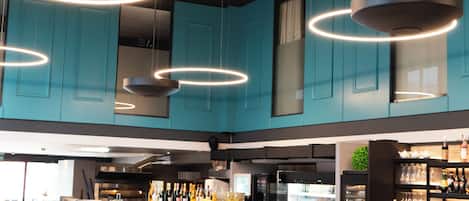 Un restaurante moderno con armarios azul verdoso, una zona de bar y una disposición de mesas y sillas.