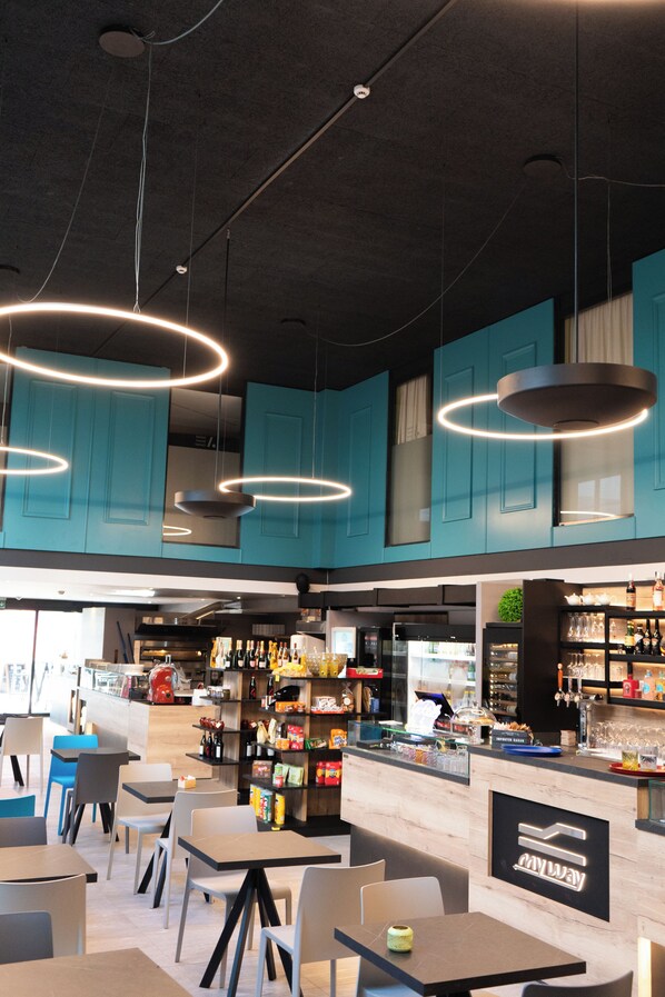 A modern restaurant with teal cabinets, a bar area, and a seating arrangement with tables and chairs.