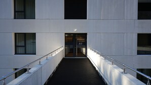 A modern building entrance with a glass door, metal railings, and a concrete pathway. - Arbed Living Hotel Self Check-in (Arbedo-Castione)