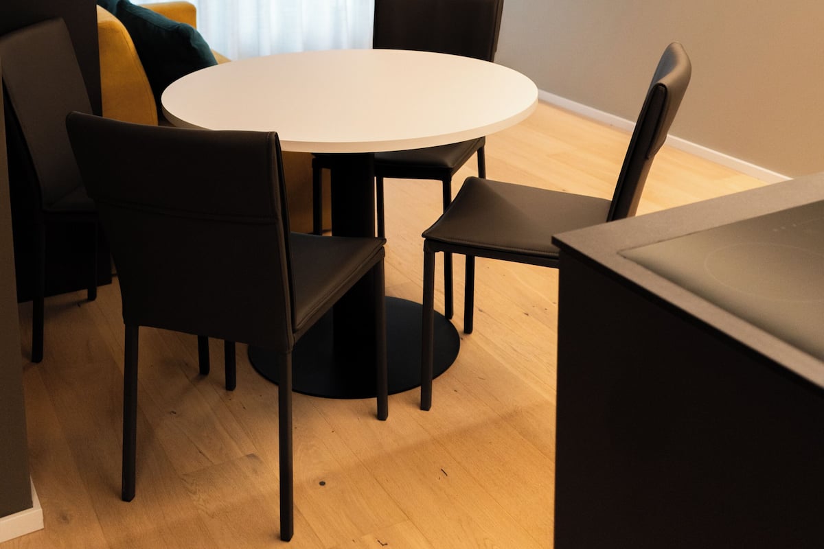 A modern dining area with a round table, black chairs, and a flat-screen TV mounted on the wall displaying a fire.