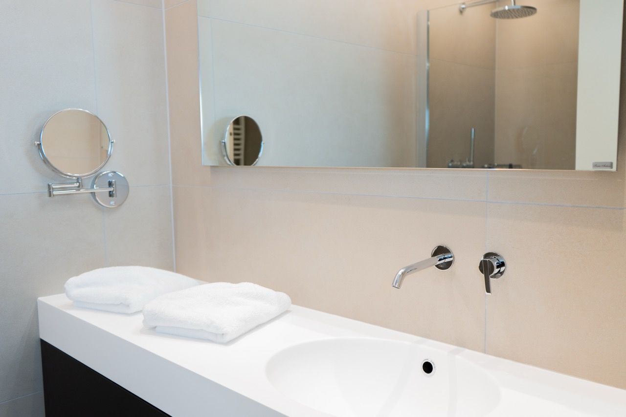 Une salle de bain moderne avec un lavabo blanc, deux miroirs et un miroir à main.