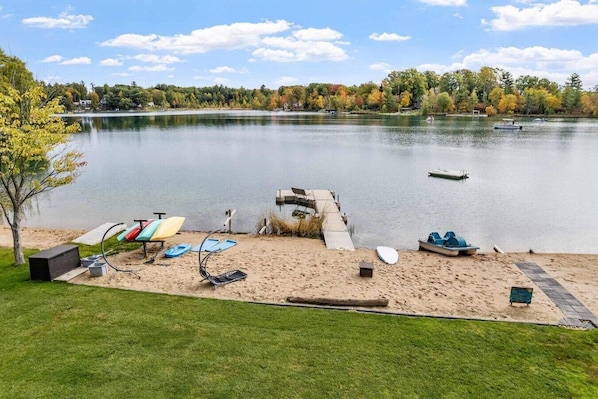 A lakeside view with a dock, boats, and a grassy area with lounge chairs and a barbecue grill. - Tiki Retreat-Hot Tub-Fire Pit - Private Beach (Sand Lake)