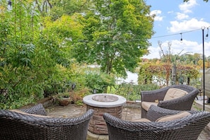 A patio with wicker furniture, a stone fire pit, and a view of a lake. - Tiki Retreat-Hot Tub-Fire Pit - Private Beach (Sand Lake)