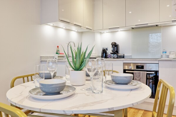 A modern kitchen with white cabinetry, a dining table set with bowls and glasses, and a coffee machine.