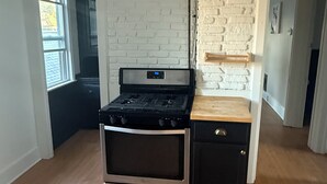 A compact kitchen with a built-in stove and oven, white brick walls, and a wooden countertop. - Cute 3BR Upper Unit Home in South Buffalo near downtown (Buffalo)