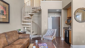 Una sala de estar con un sofá de cuero marrón, un sillón gris, una mesa de centro de madera y una escalera en espiral.