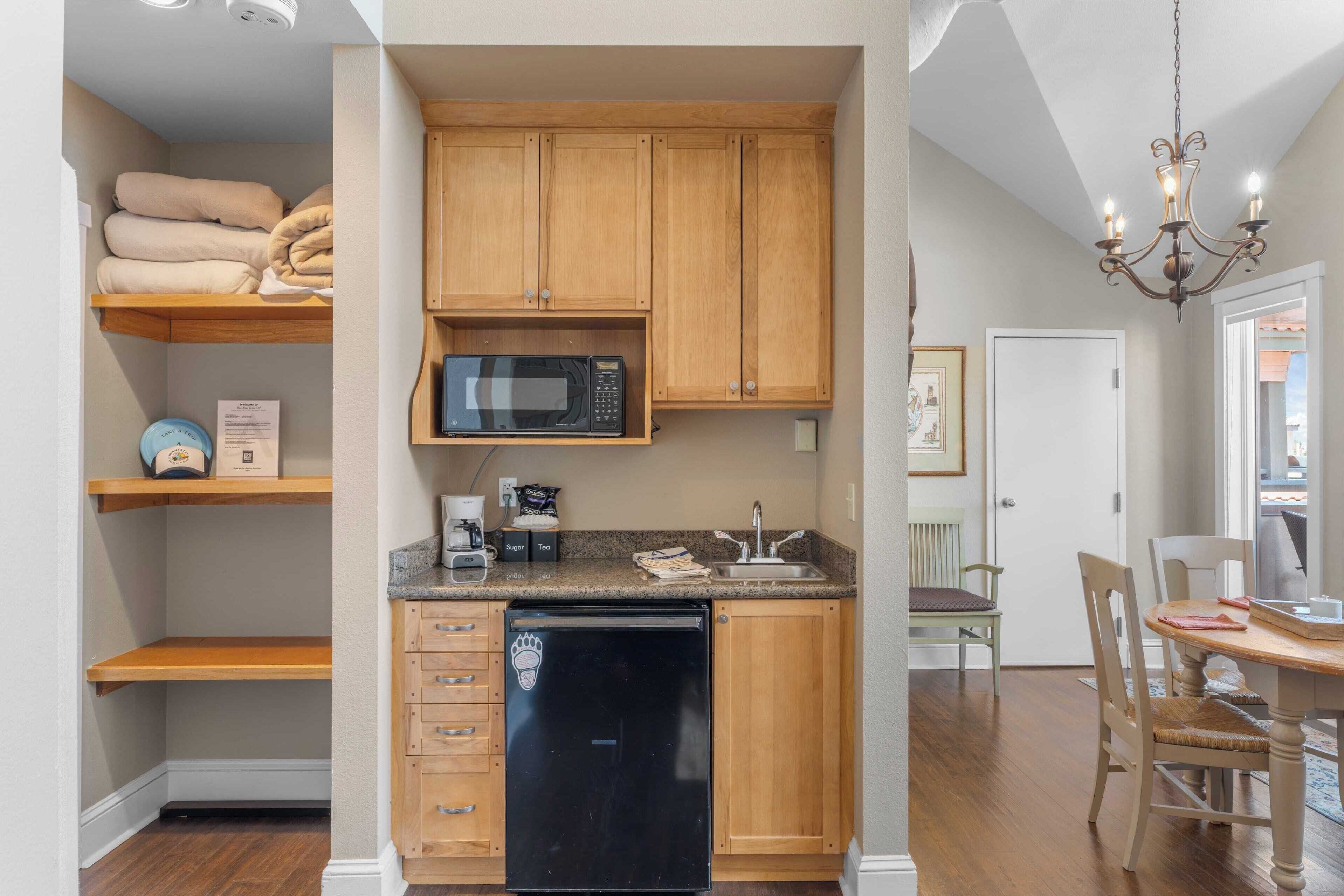 A compact kitchen with wooden cabinets, a microwave, a coffee maker, and a dishwasher.
