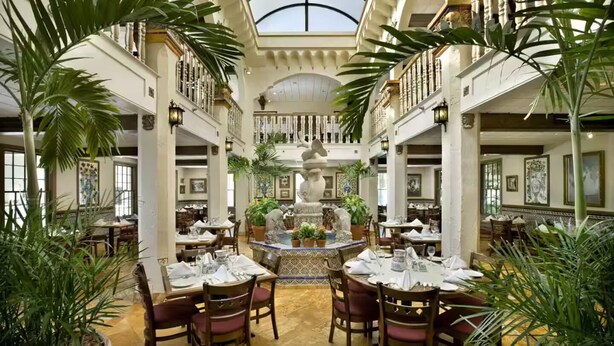 Une salle à manger spacieuse et élégante, dotée de nombreuses tables et chaises, entourée d’une végétation luxuriante et agrémentée d’une fontaine centrale.