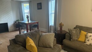 Uma sala de estar com um sofá cinzento, um tapete estampado e um espaço de jantar com uma mesa e cadeiras.