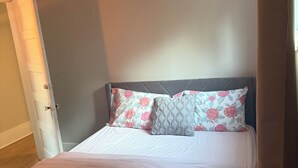 Quarto com cama, roupa de cama estampada, cabeceira escura e porta à esquerda.