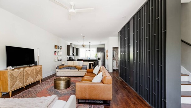 Una sala de estar moderna con un sofá, un televisor y un comedor al fondo.