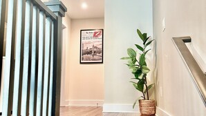 Una escalera de madera con barandilla metálica que conduce a un rellano con un cuadro enmarco y una planta en maceta.