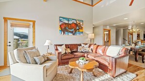 A spacious living room with a large sectional sofa, a coffee table, and a painting of a moose. - Walk to Town Center Shops & Restaurants, Private Hot Tub, 3BR + Loft (Big Sky)