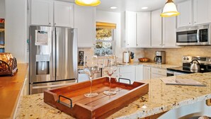 A modern kitchen with white cabinets, stainless steel appliances, and a wooden serving tray with wine glasses. - Walk to Town Center Shops & Restaurants, Private Hot Tub, 3BR + Loft (Big Sky)