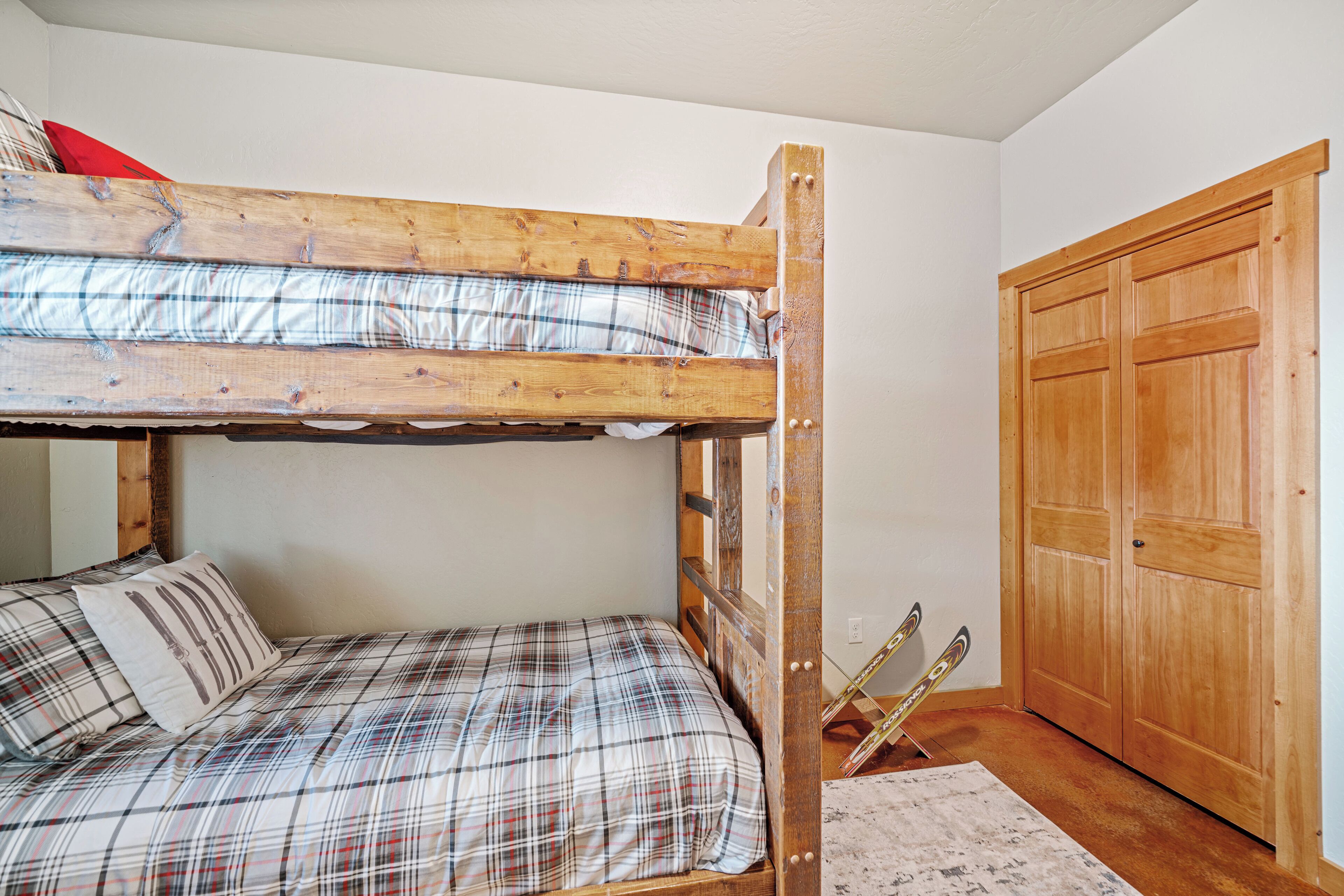 Een stapelbed met geruite beddengoed, een houten deur en ski's die tegen de muur staan.