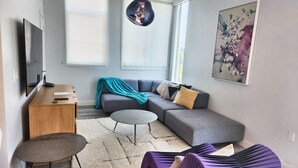 A modern living room with a grey sofa, a small round table, a purple chair, and a large window with a view.