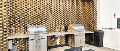 An outdoor barbecue area with two grills, a sink, and a trash bin.
