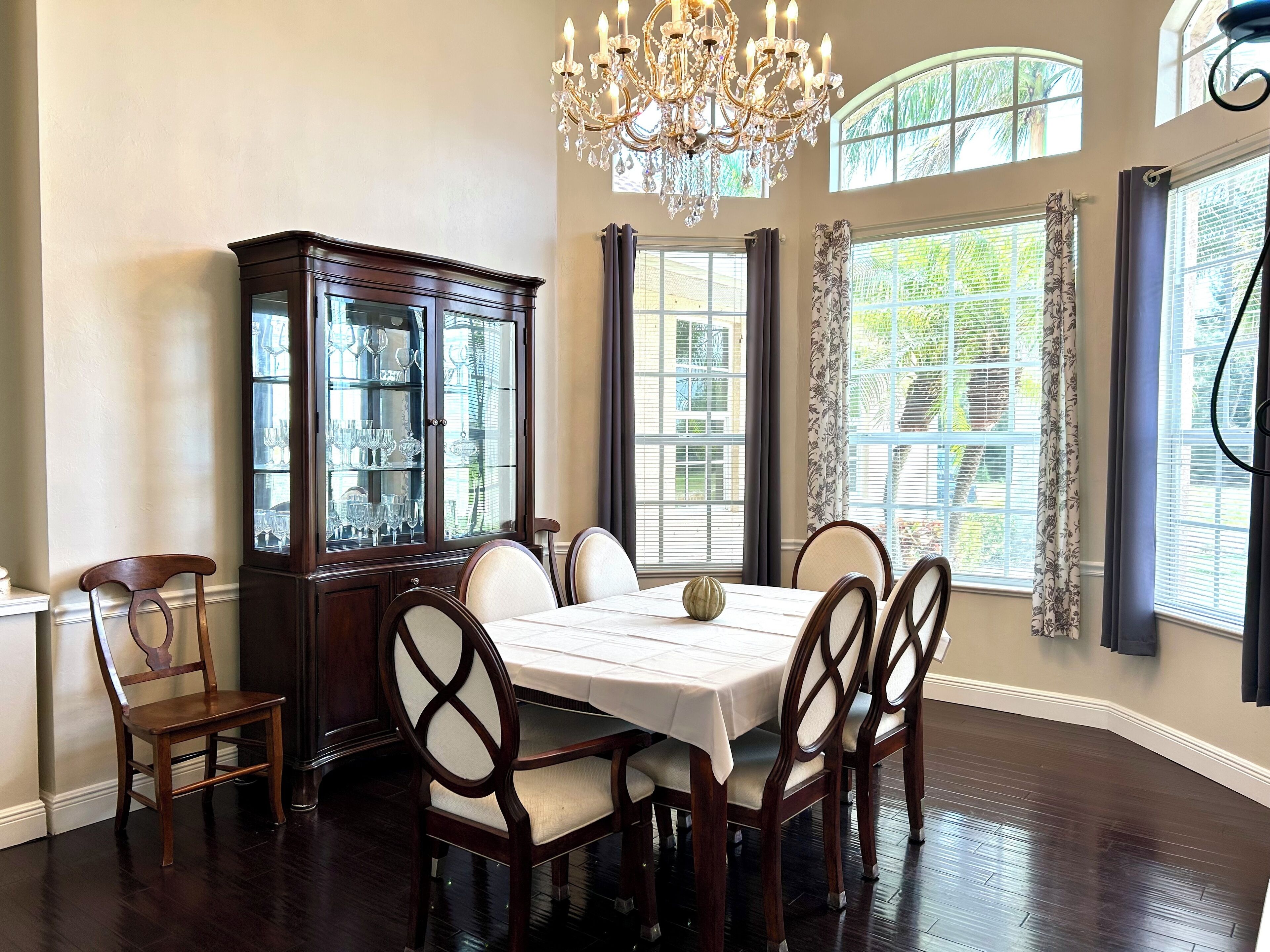 A dining room with a dark wood table, six chairs, a glass-fronted china cabinet, and a chandelier.