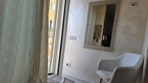 Une pièce avec une chaise blanche, un miroir au mur et un rideau à motifs.