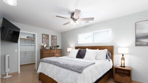 Un dormitorio moderno con una cama de madera, un ventilador de techo, un televisor y una ventana con persianas.