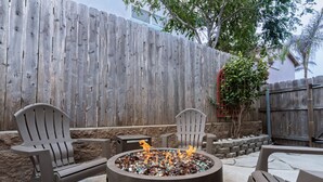Una chimenea con sillas alrededor, una cerca de madera y un muro de piedra al fondo.