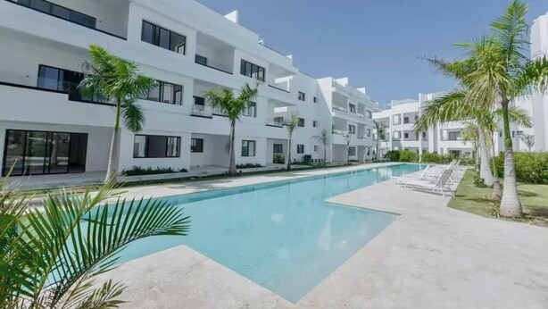A modern building with a swimming pool, surrounded by palm trees and a clear sky. - Penthouse with private jacuzzi, beach access, perfect for long stays! (Punta Cana)