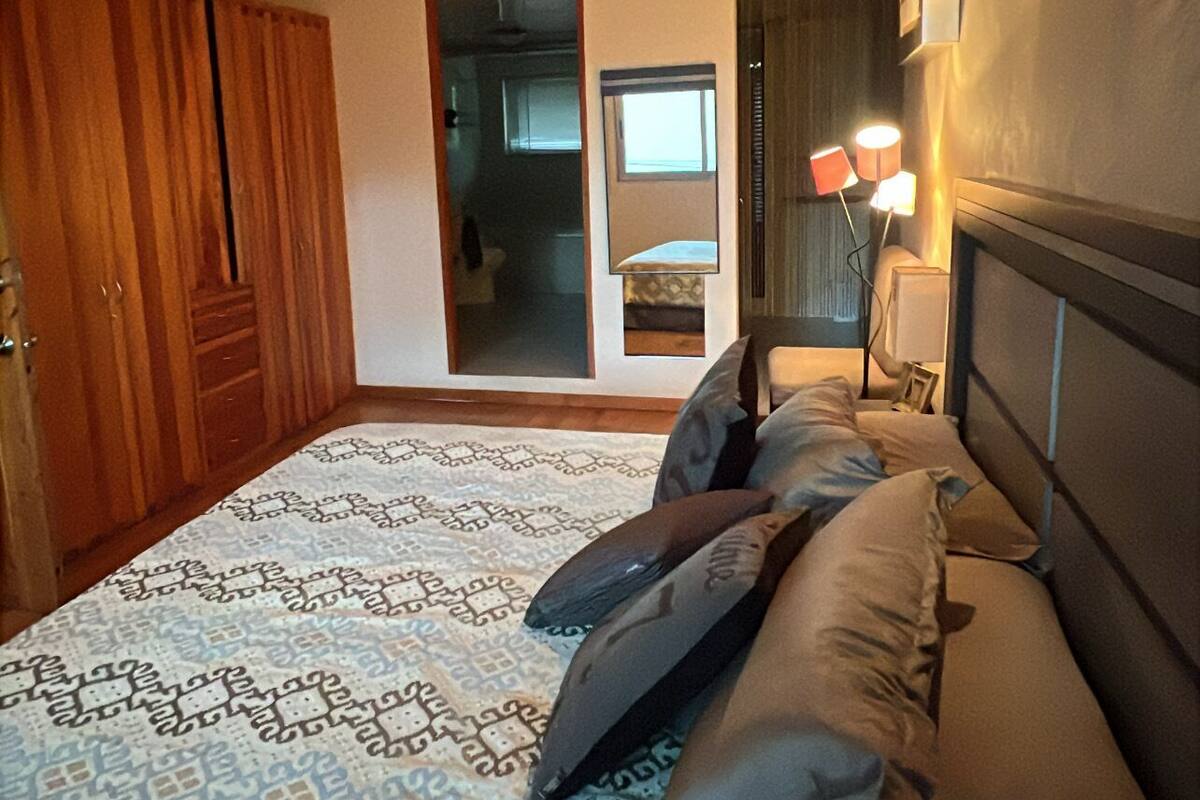 A bedroom with a wooden ceiling, a patterned bedspread, and a nightstand with a lamp.