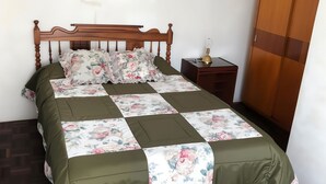 A neatly made bed with a floral bedspread and green curtains, a wooden wardrobe, and a small bedside table with a lamp. - One-bedroom French style apartment in downtown Ambato (Ambato)