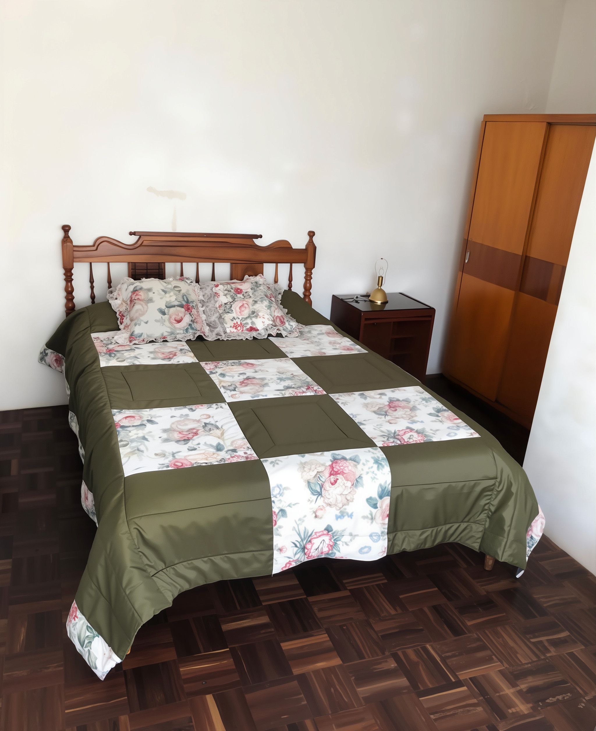 A neatly made bed with a floral bedspread and green curtains, a wooden wardrobe, and a small bedside table with a lamp.