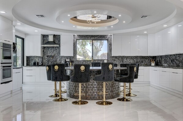 Una cocina moderna con una isla central, muebles blancos y un diseño de techo circular.