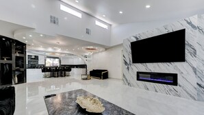 Amplia sala de estar con una cocina moderna, un televisor de pantalla plana grande montado en una pared de mármol y una original mesa de centro de mármol blanco y negro.