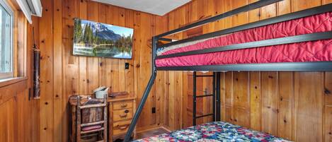 Una cama individual con un edredón colorido, paredes de madera, un escritorio con una silla y un cuadro de un paisaje montañoso.