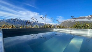 Ein klares, blaues Infinity-Pool mit Blick auf schneebedeckte Berge und einen wolkenlosen Himmel.