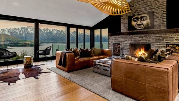 Ein modernes Wohnzimmer mit Kamin, Ledersofas und einem großen Fenster mit Blick auf eine Berglandschaft.