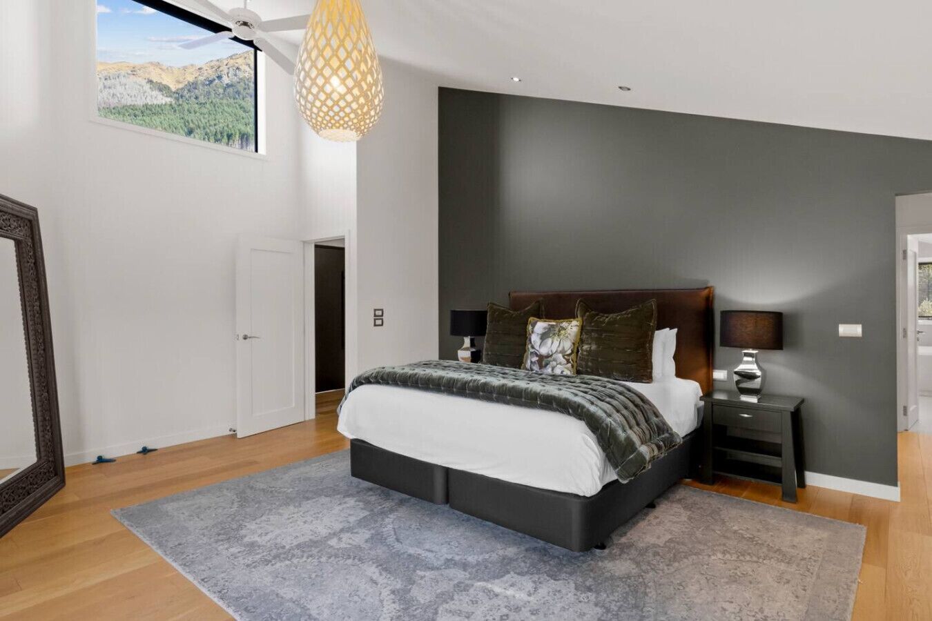 A bedroom with a large bed, a nightstand, a lamp, and a view of a mountainous landscape through a window.