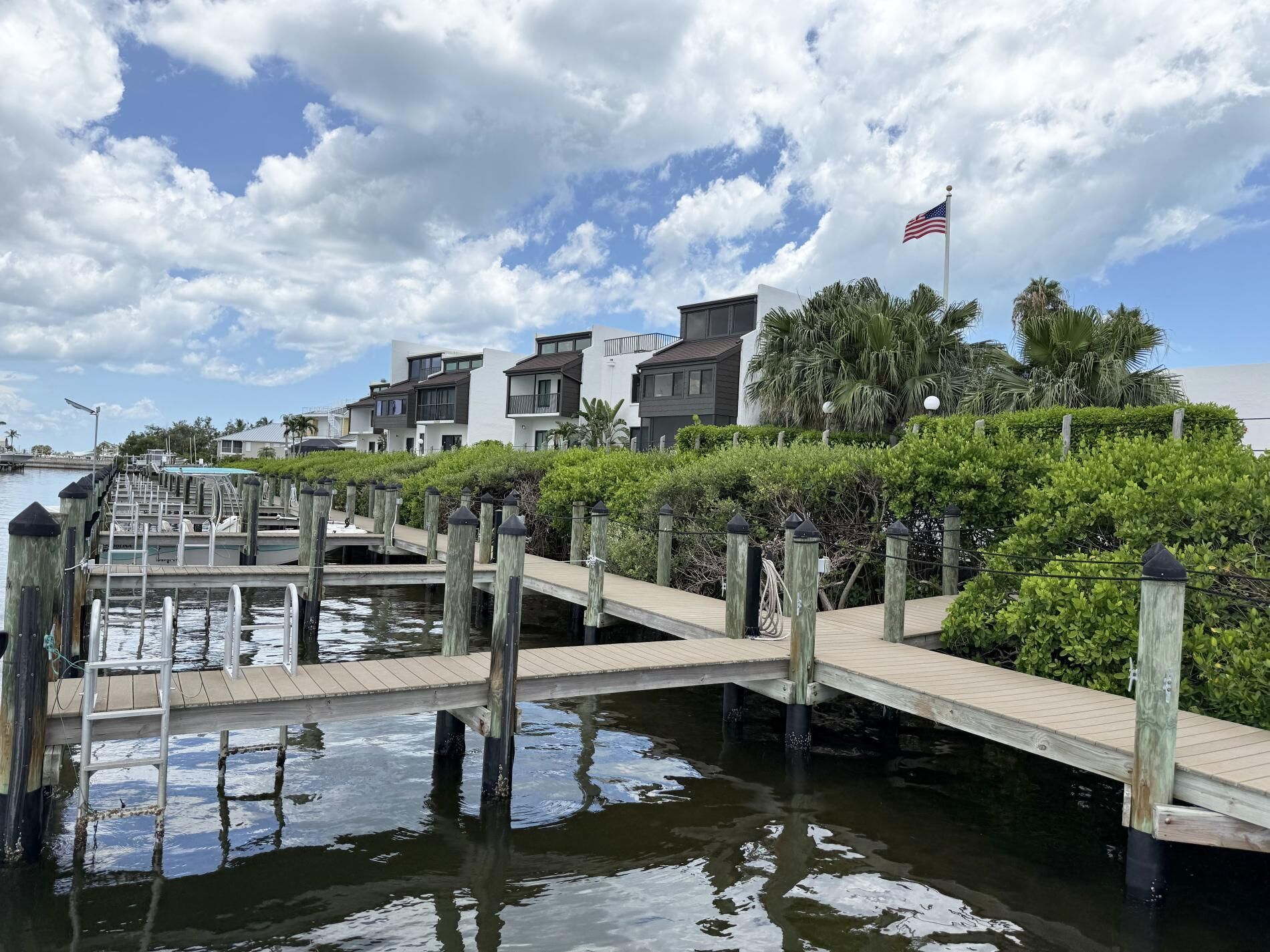 Una propiedad frente al agua con muelle, un pequeño puente y edificios modernos con balcones.